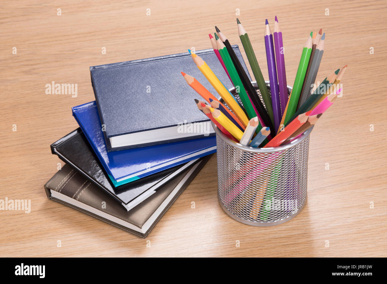 Pile of planners lying by colored pencils in stand on wooden desk Stock Photo