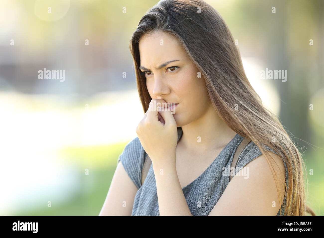 Nervous woman biting nails and looking away alone outdoors in the street Stock Photo