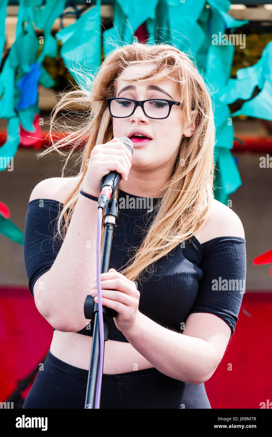 England, Ramsgate. Young blond woman singer songwriter, Dannie Jayne singing on stage, daytime, outdoors. Front view. Stock Photo