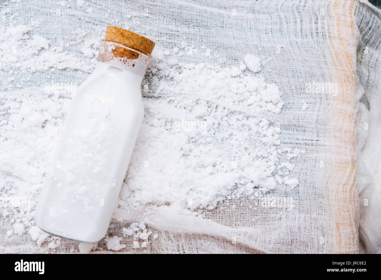 Homemade coconut milk in a bottle, mixed in a blender and pressed through a cotton sieve, over a coconut essicated powder on a white background Stock Photo