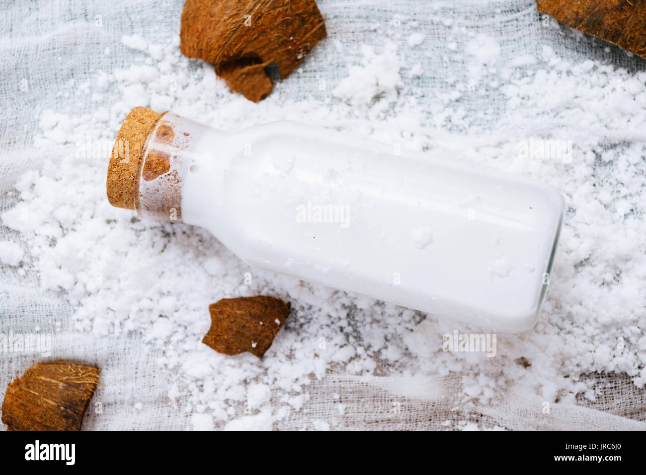 Homemade coconut milk in a bottle, mixed in a blender and pressed through a cotton sieve, over a coconut essicated powder on a white background Stock Photo