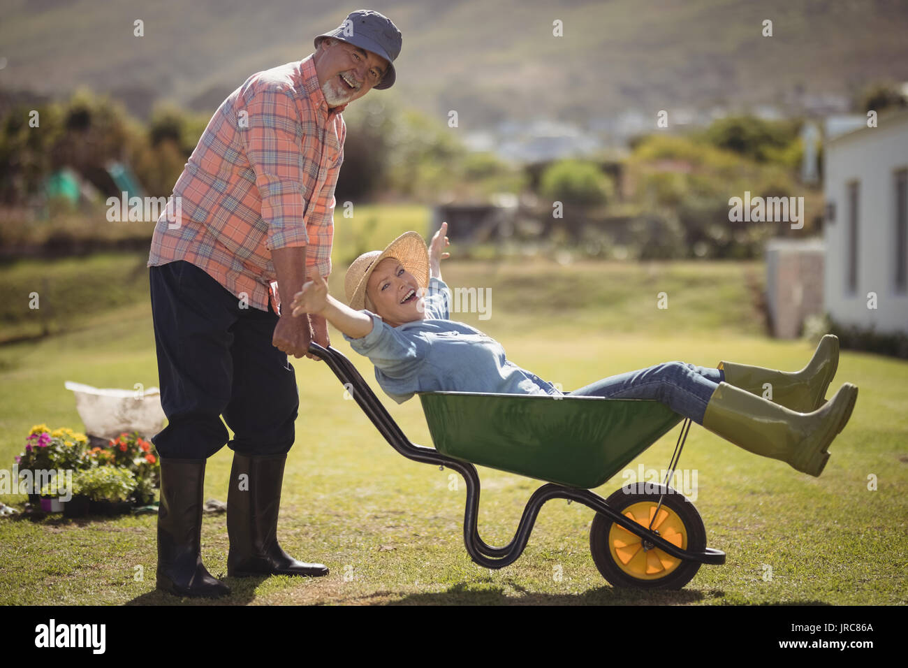 Portrait of senior man giving woman ride in wheelbarrow on a sunny day Stock Photo