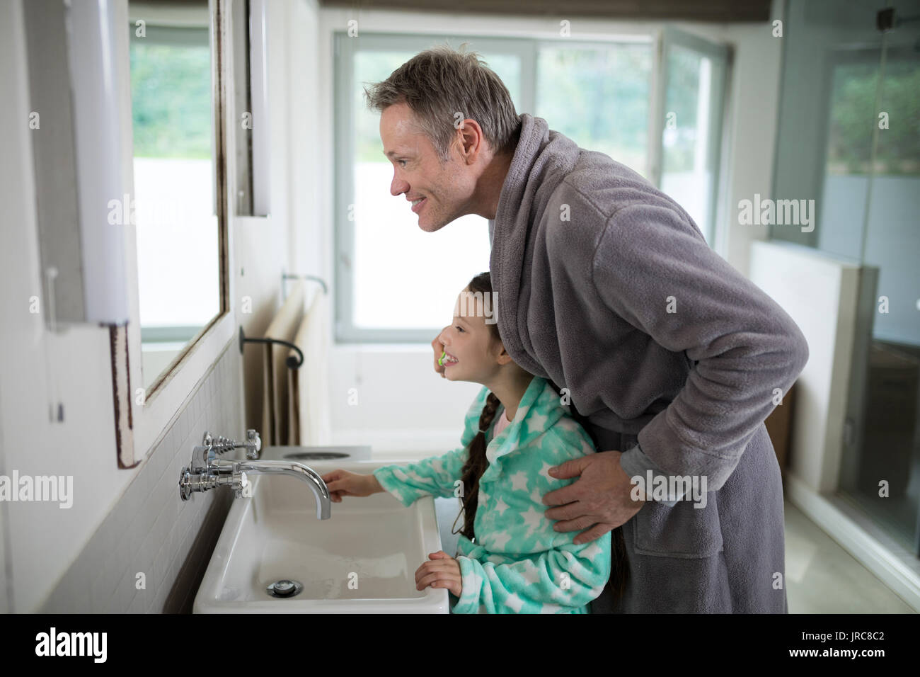 Father and daughter brushing teeth in bathroom at home Stock Photo