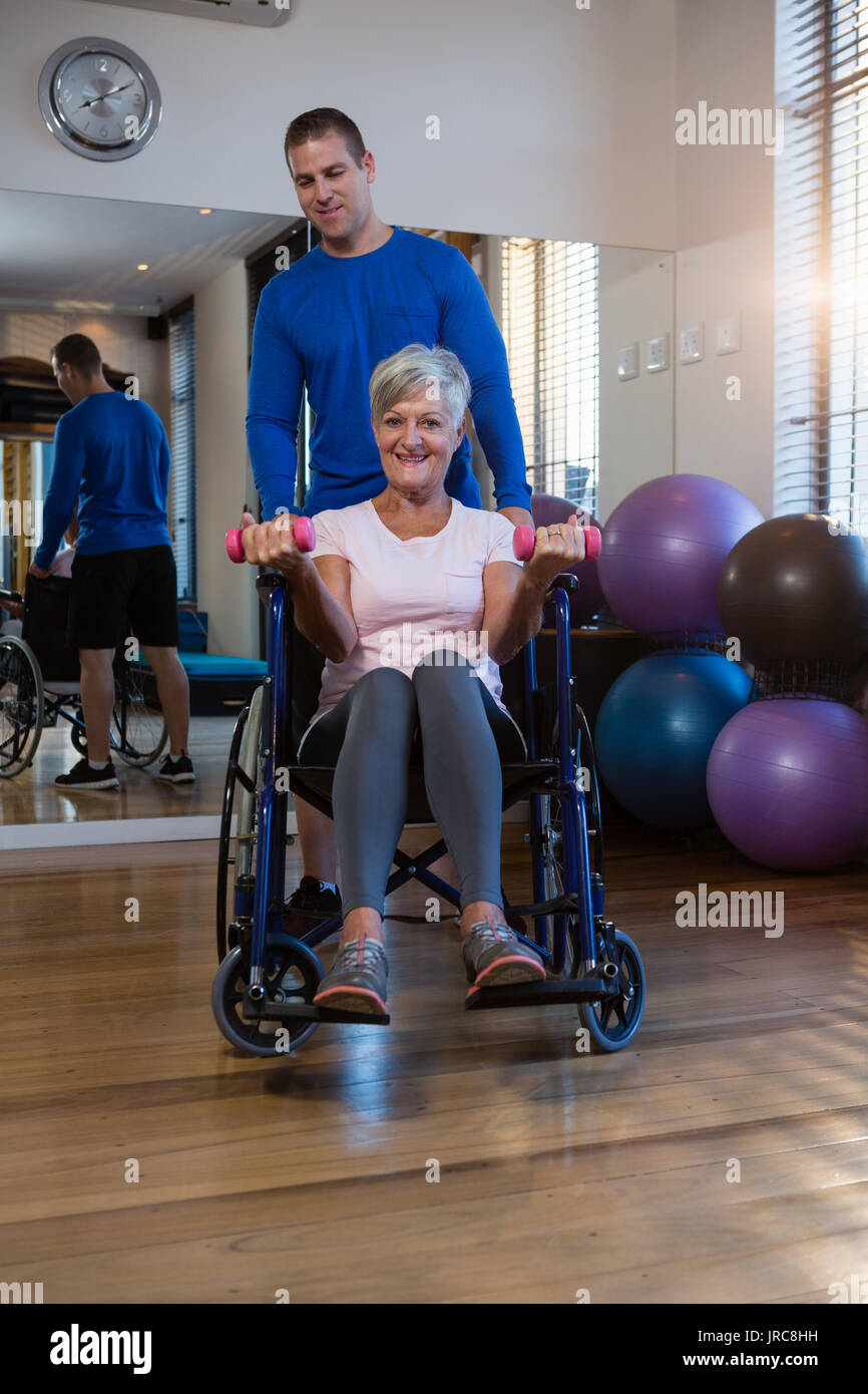 Portrait of male physiotherapist helping patient in performing exercise with dumbbell in clinic Stock Photo