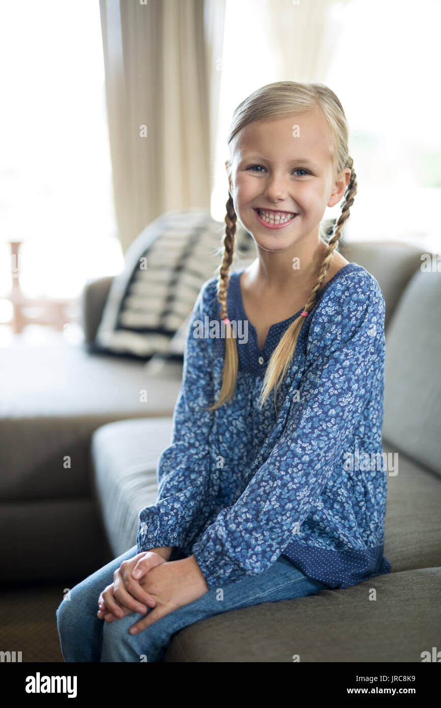 Portrait of smiling girl sitting on sofa in living room at home Stock ...