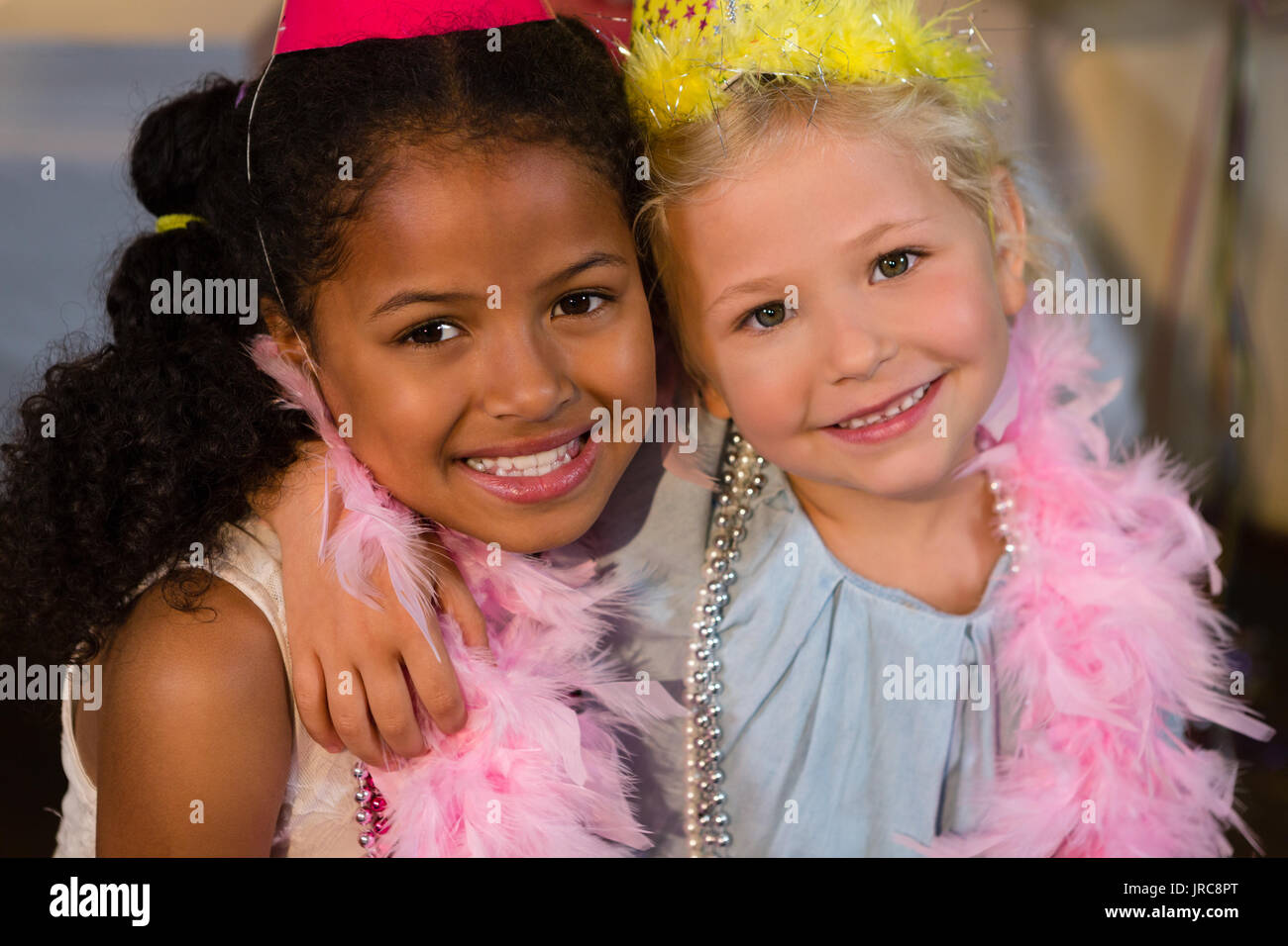 Portrait of smiling girls with arm around wearing feather boa Stock Photo