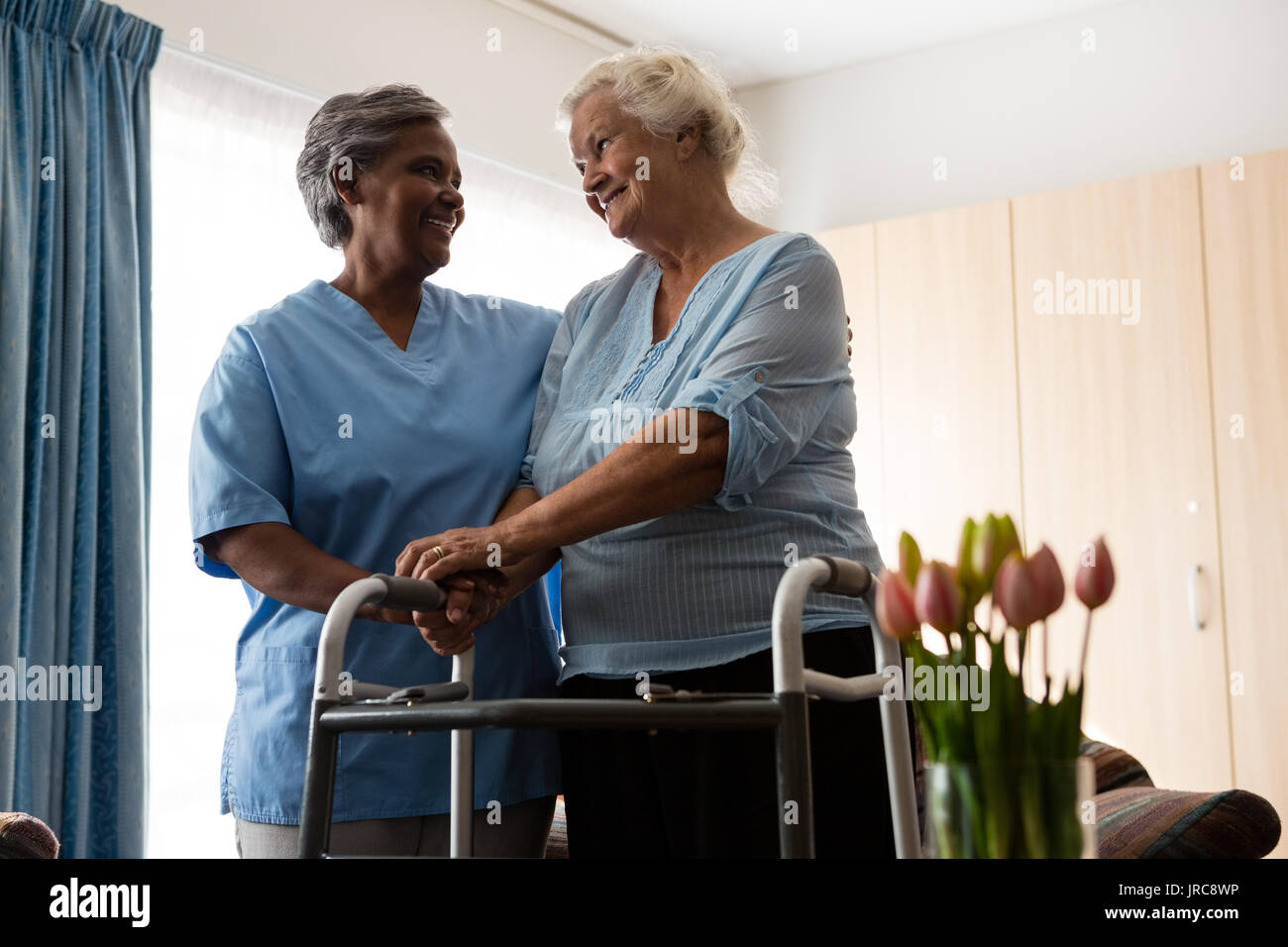 Nurse assisting senior patient in walking with walker at nursing home