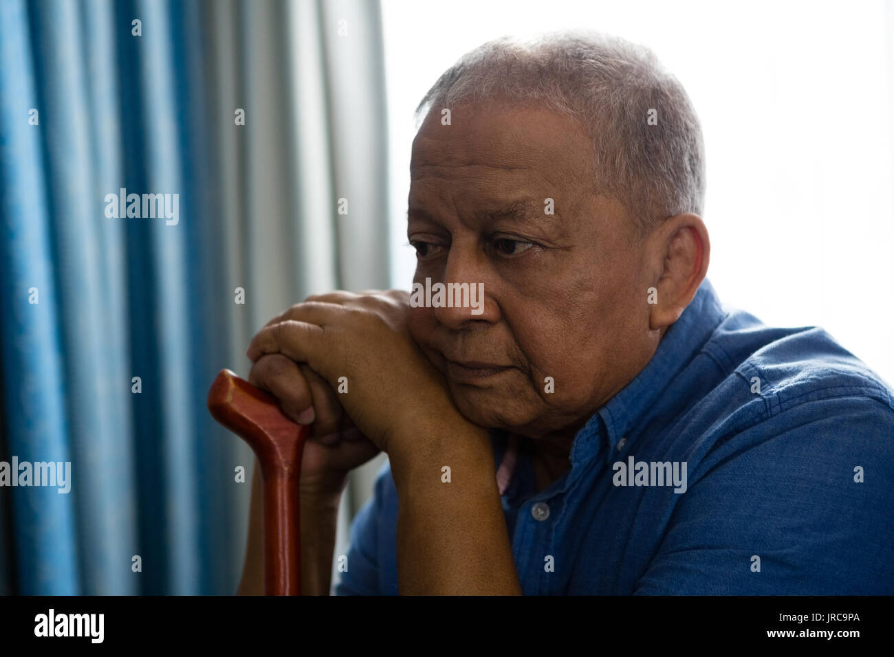 Thoughtful sad senior man with walking cane sitting by window in nursing home Stock Photo