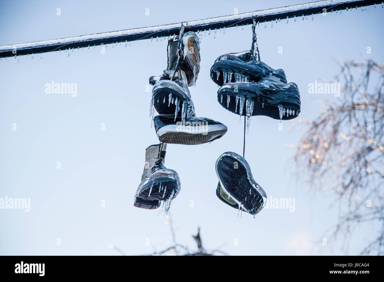 Shoes tied together by their laces are hanging from a line. But after an Ice storm, they are covered with a thick layer of ice, forming many icicles Stock Photo