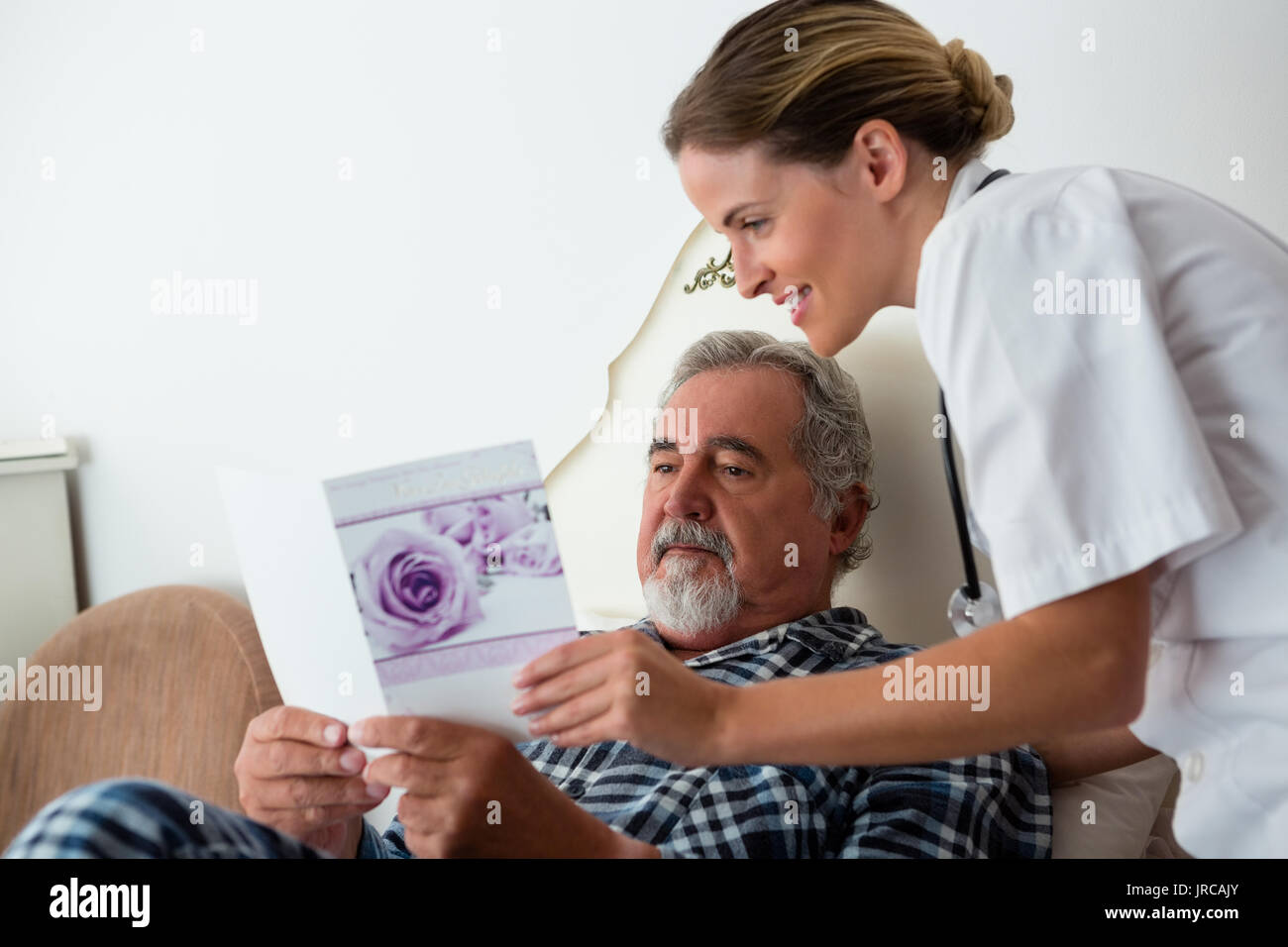 Female doctor showing get well card to patient relaxing on bed in
