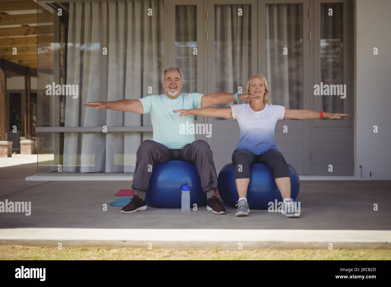 Senior couple doing stretching exercise on exercise ball at veranda ...