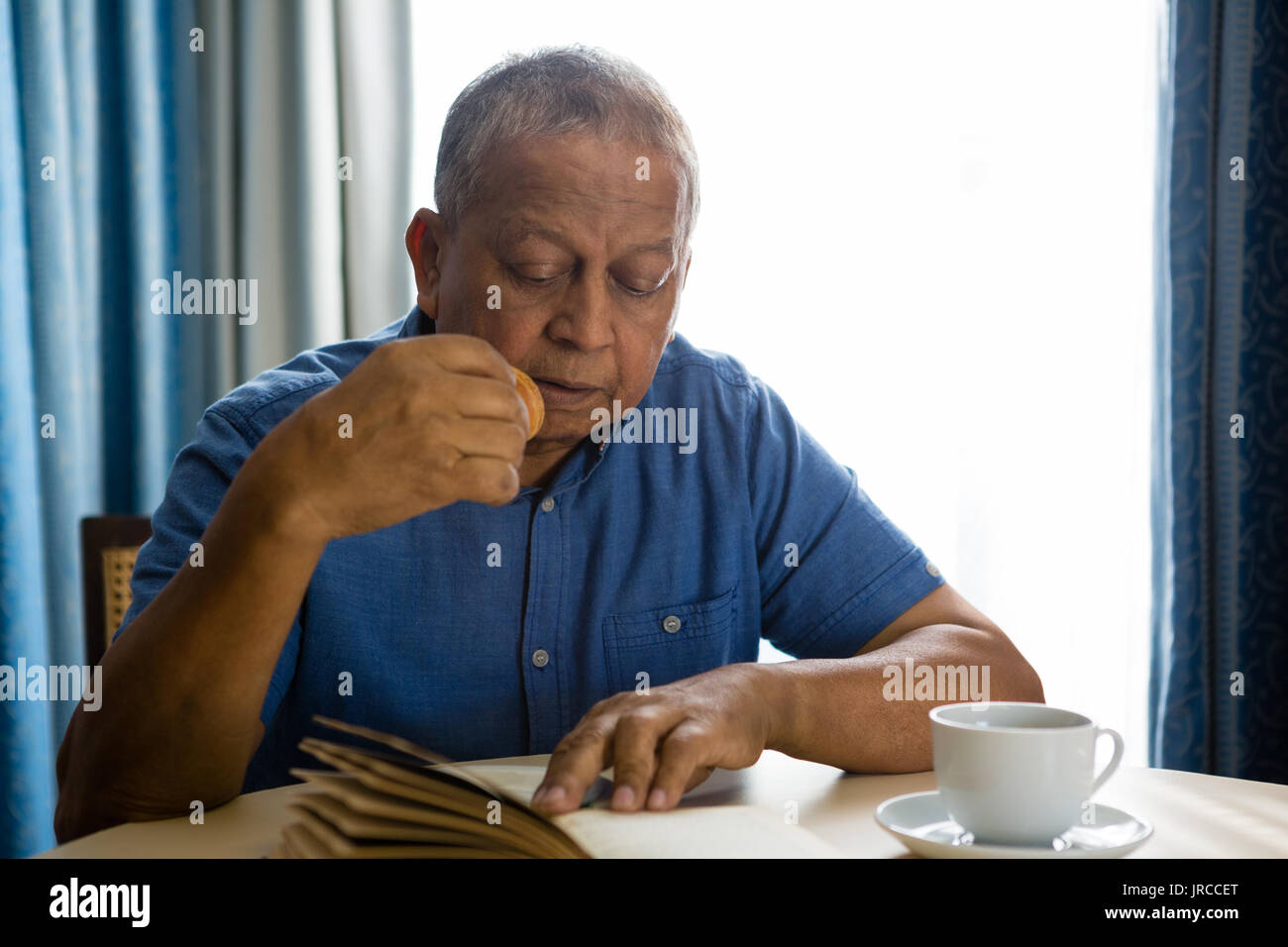 Senior man eating food while reading book at table in nursing home Stock Photo