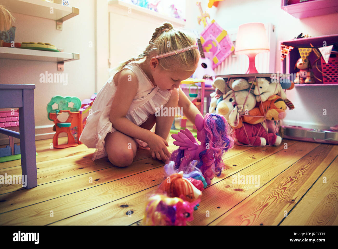 Thoughtful little girl putting toys in line on the floor. Horizontal indoors shot. Stock Photo