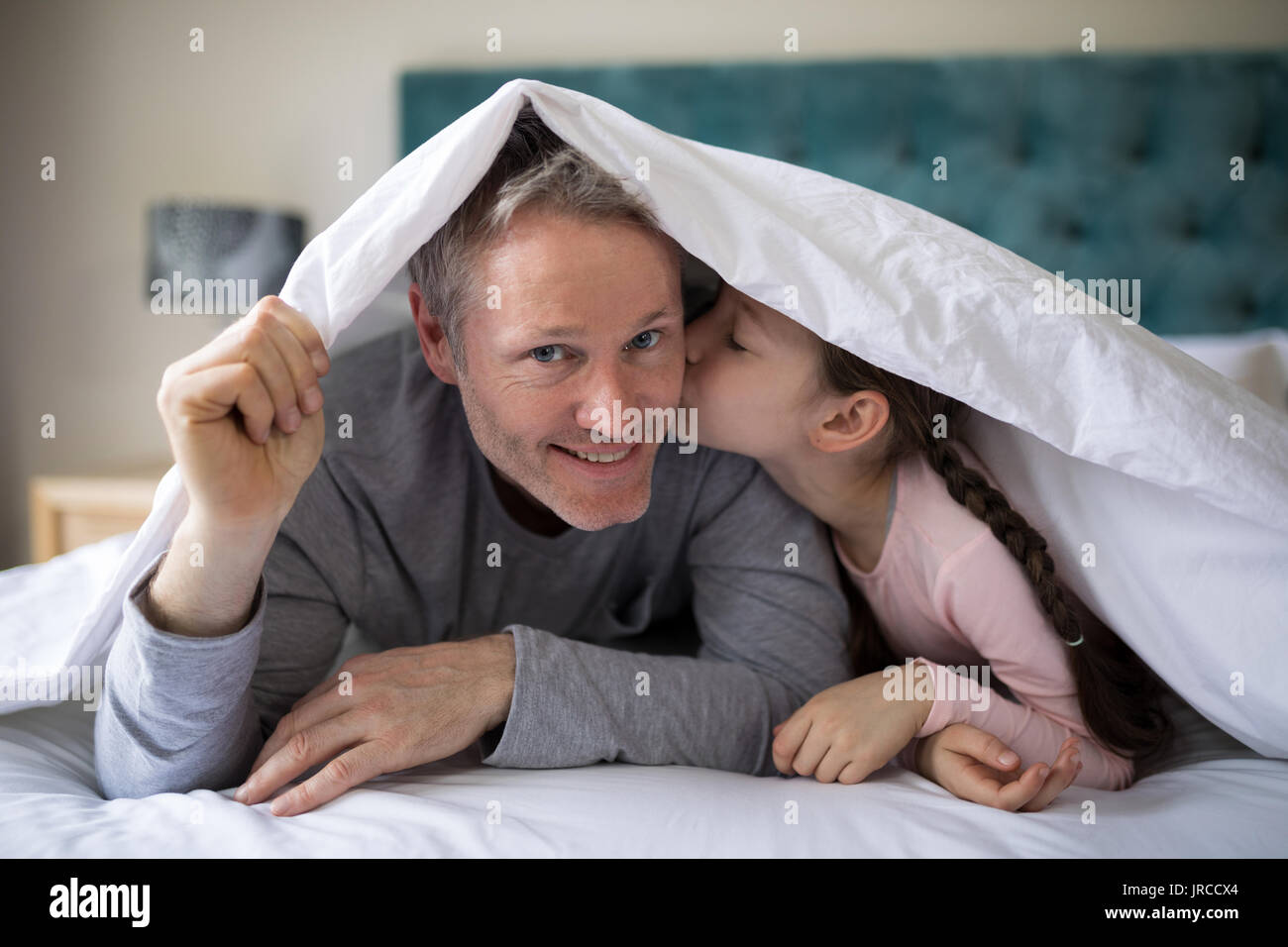 Little girl kissing her father on chick in bedroom Stock Photo