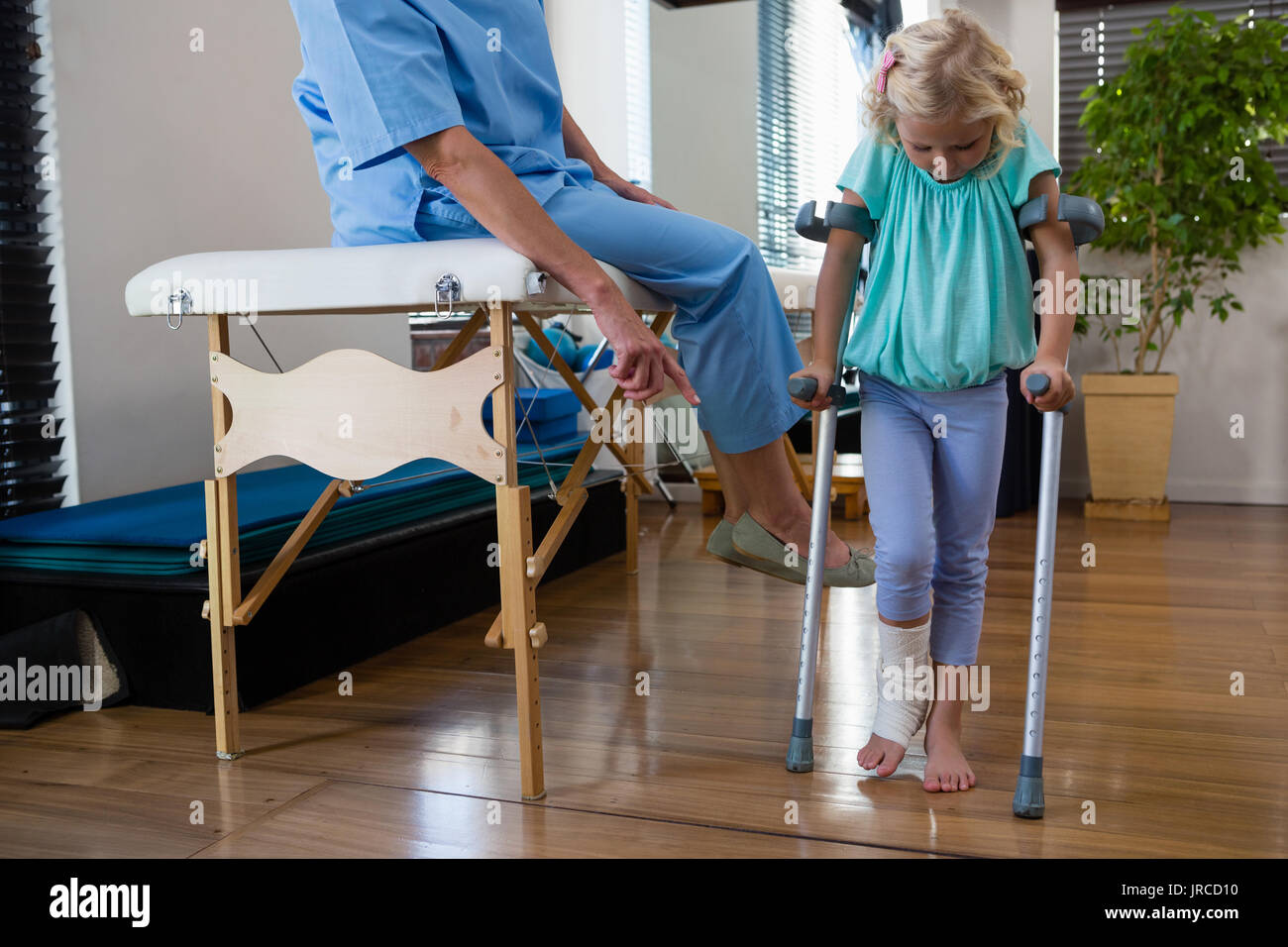 Physiotherapist assisting girl patient to walk with crutches in clinic