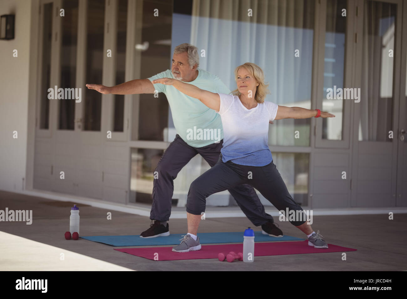 Senior couple performing stretching exercise at veranda Stock Photo - Alamy