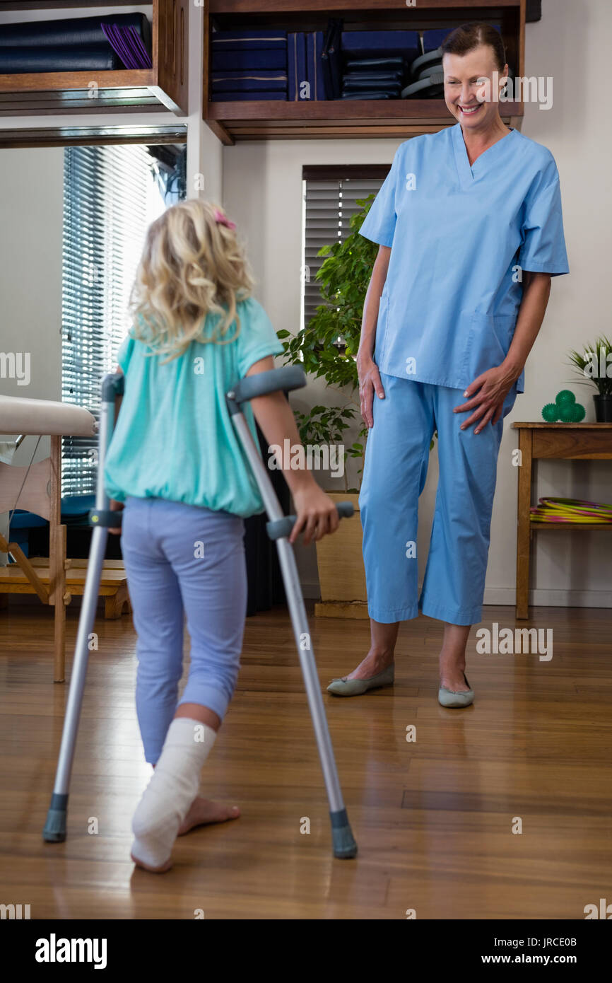Physiotherapist assisting girl patient to walk with crutches in clinic