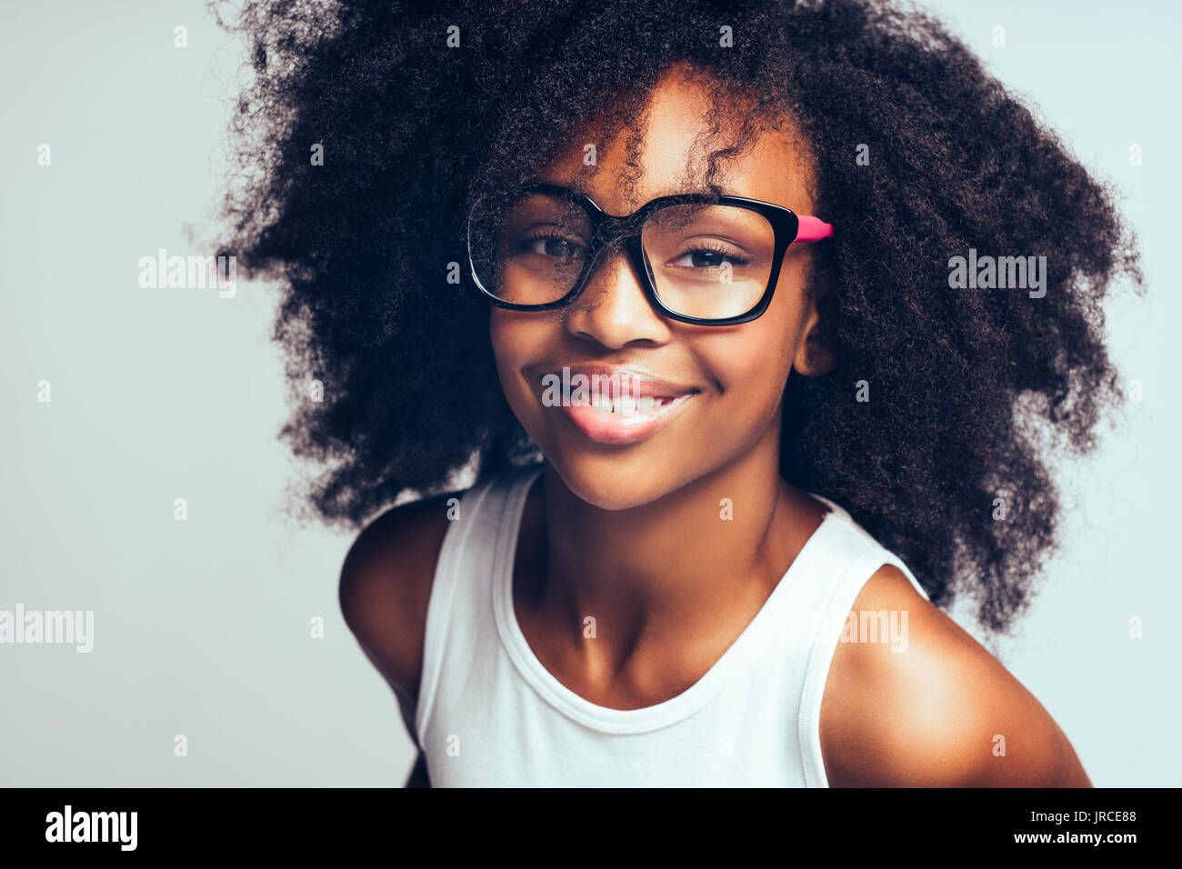 Smiling young African girl with long curly hair wearing glasses while ...
