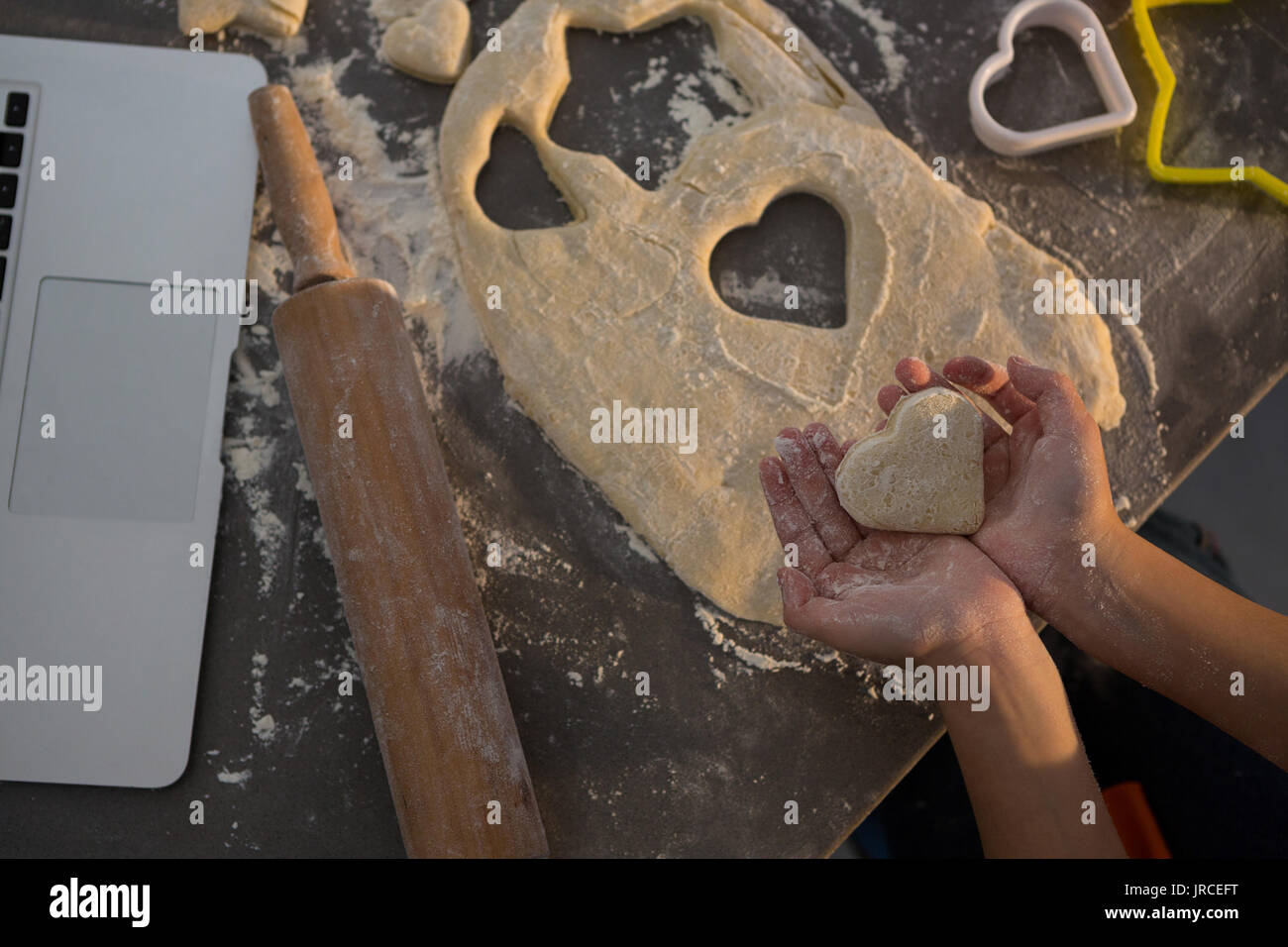 Cropped hands of girl holding heart shape dough at kitchen counter Stock Photo