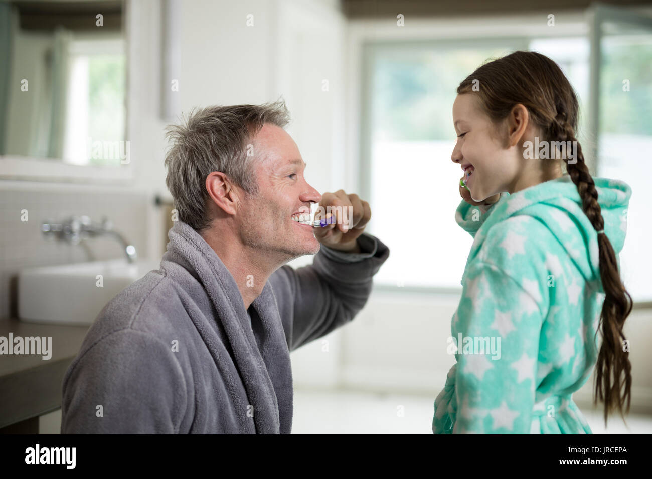 Smiling father and daughter brushing teeth in bathroom at home Stock Photo