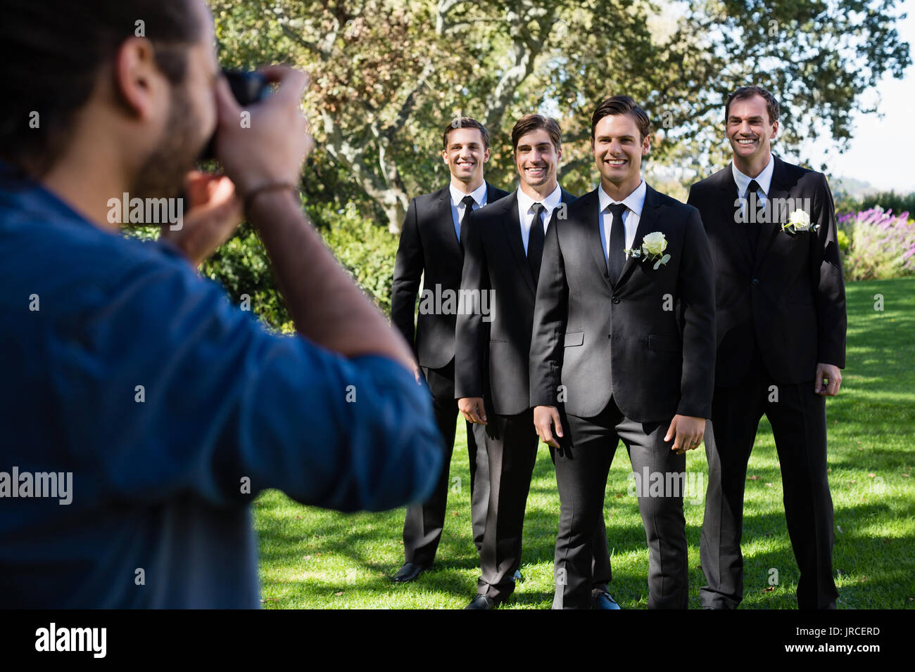 Photographer taking photo of groom and groomsmen at park Stock Photo
