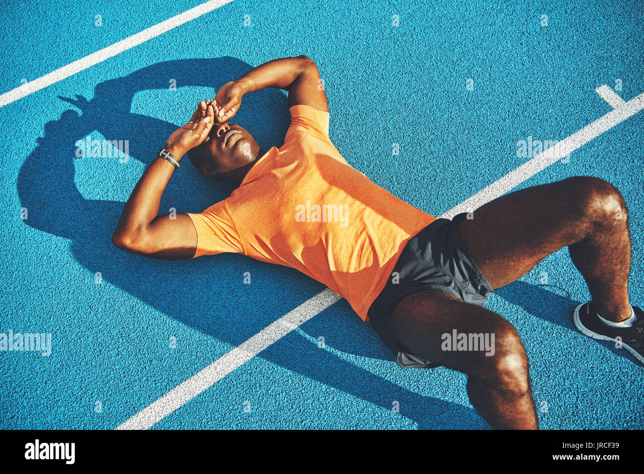 Tired young athletic African man in sportswear lying on the lanes of a running track taking a break from training Stock Photo