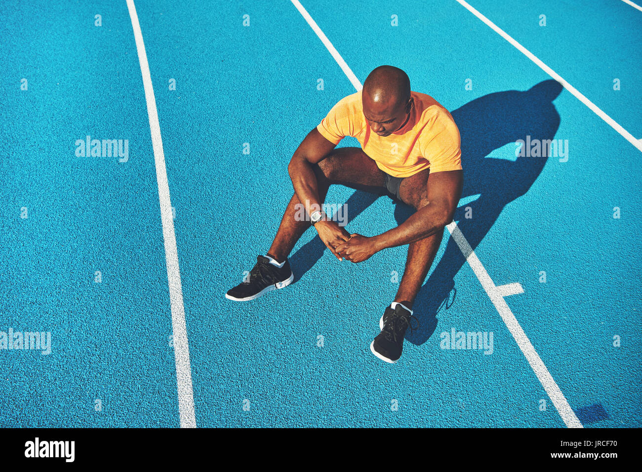 Young African male athlete in sportswear sitting alone on the lanes of a running track on a sunny day Stock Photo
