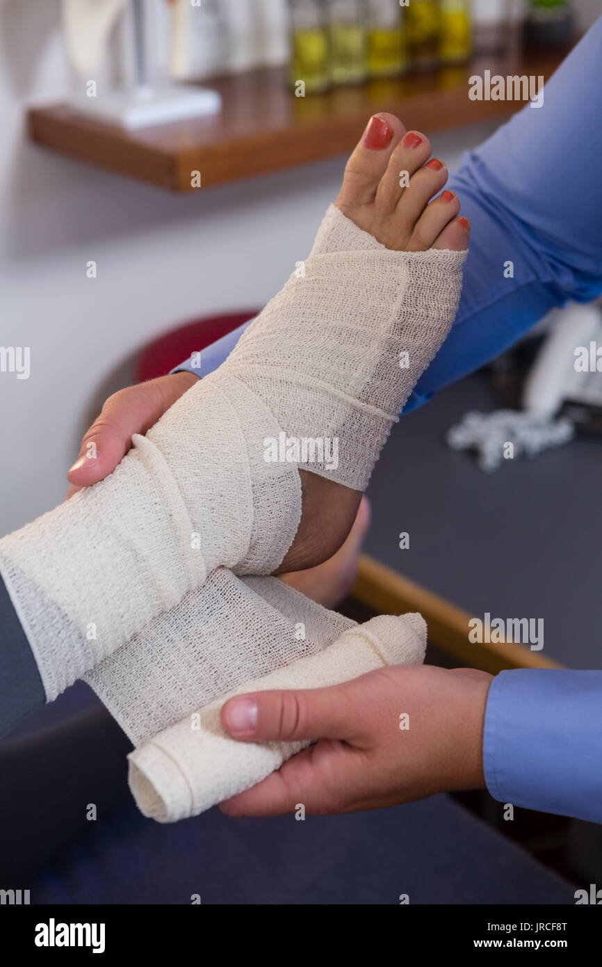 Physiotherapist putting bandage on injured feet of patient in clinic
