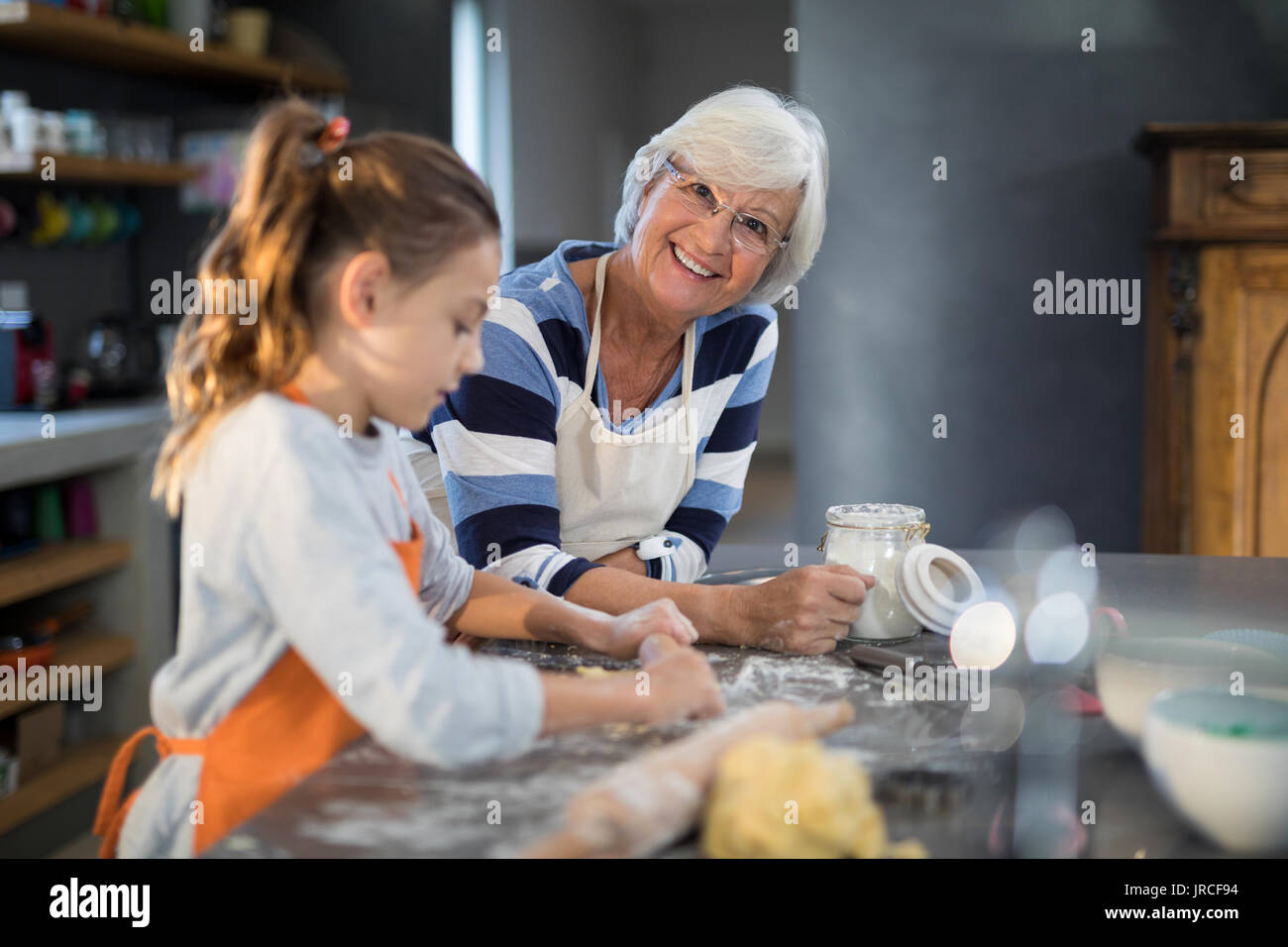 Granddaughter flattening dough with grandmother in the kitchen Stock Photo