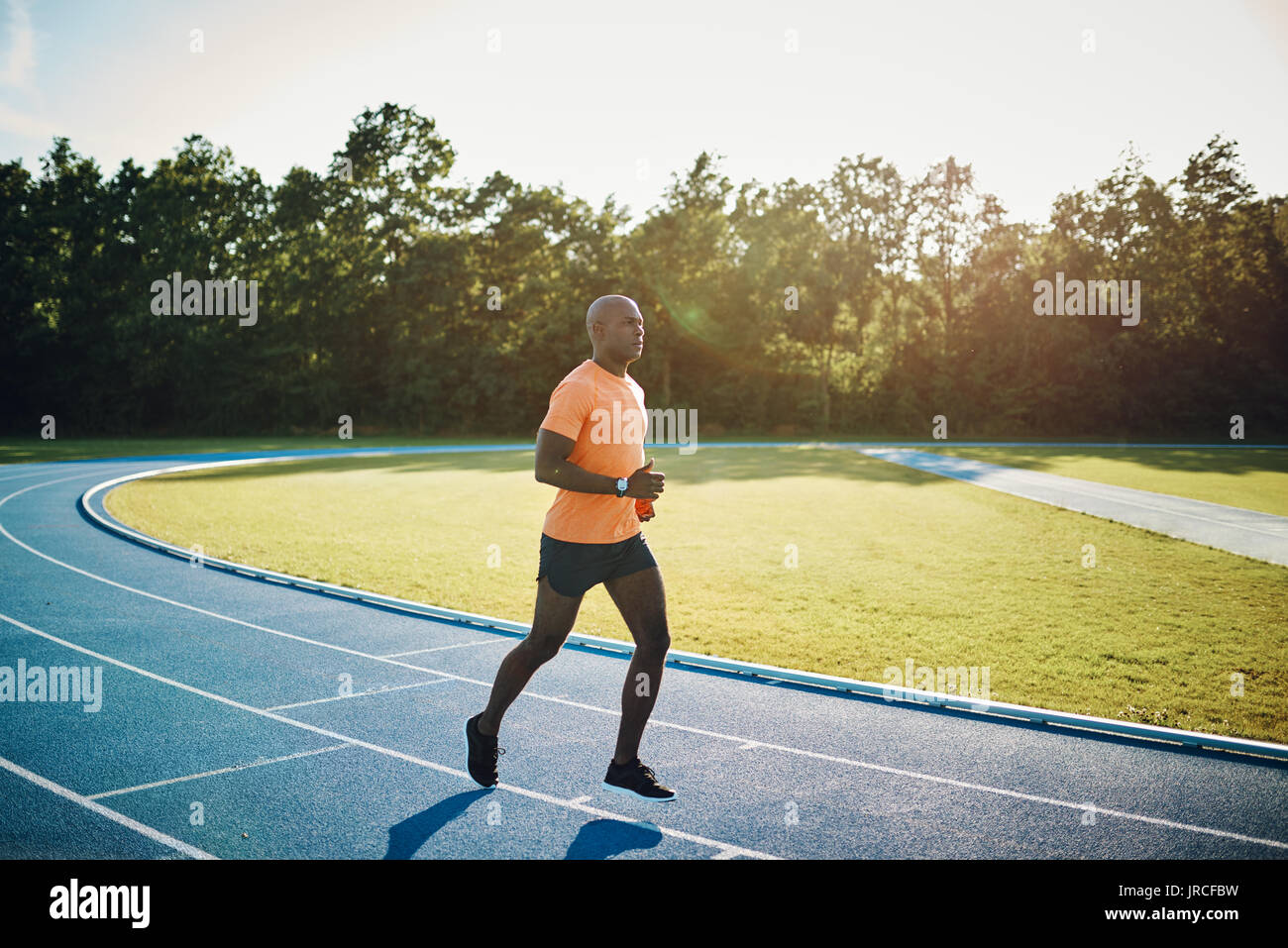 Focused young African male athlete in sportswear running alone along a race track on a sunny day Stock Photo