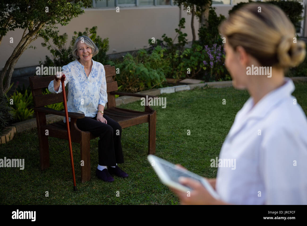 Female doctor holding tablet looking at woman sitting on bench in park ...