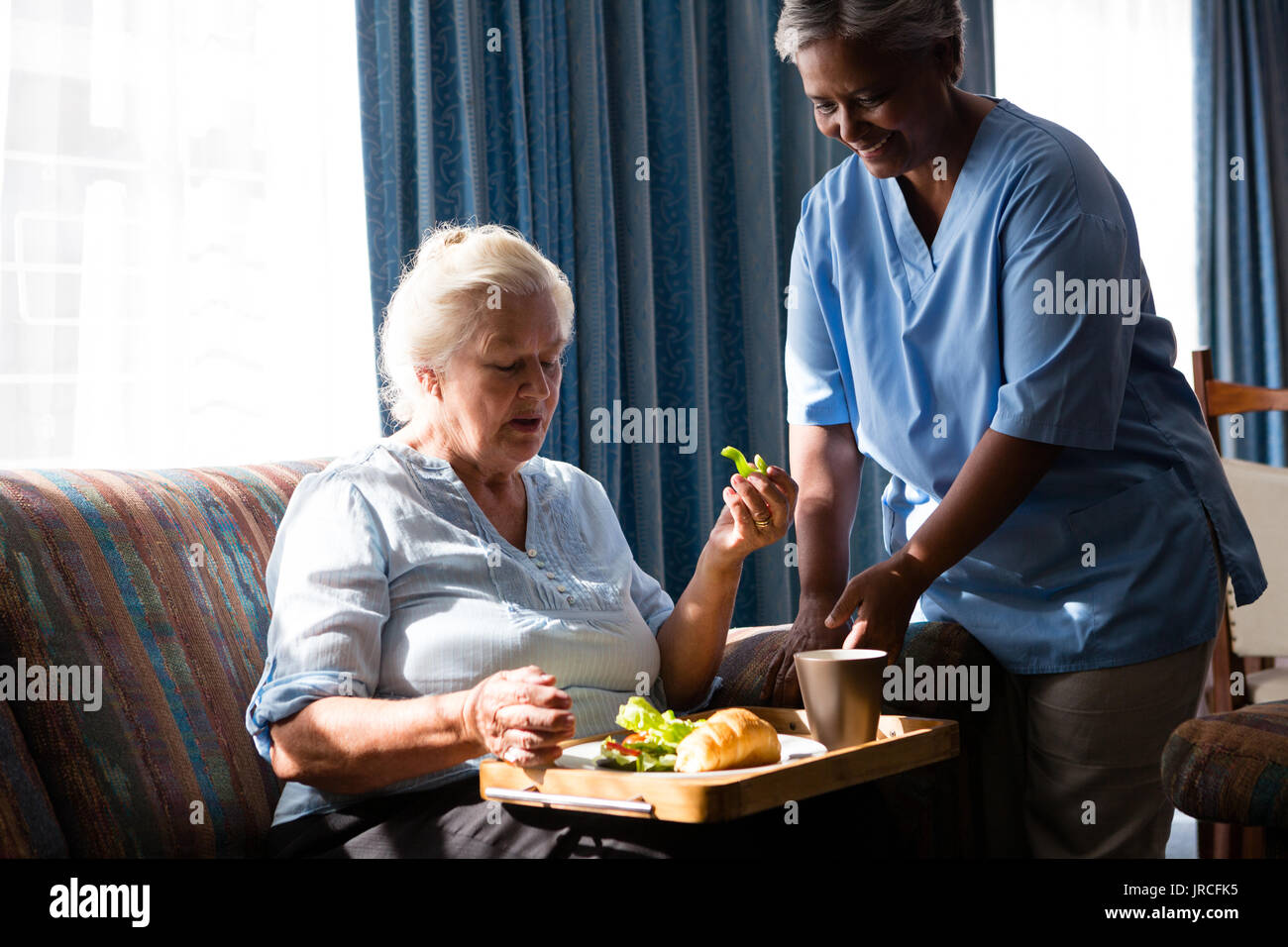 Doctor standing by senior woman eating food at table in nursing home Stock Photo