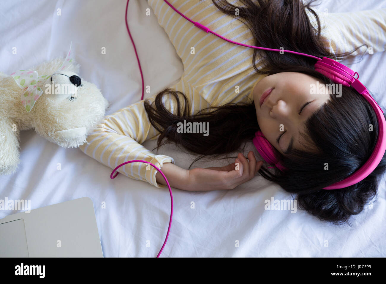 Girl With Toy Listening To Music While Sleeping On Bed At Home