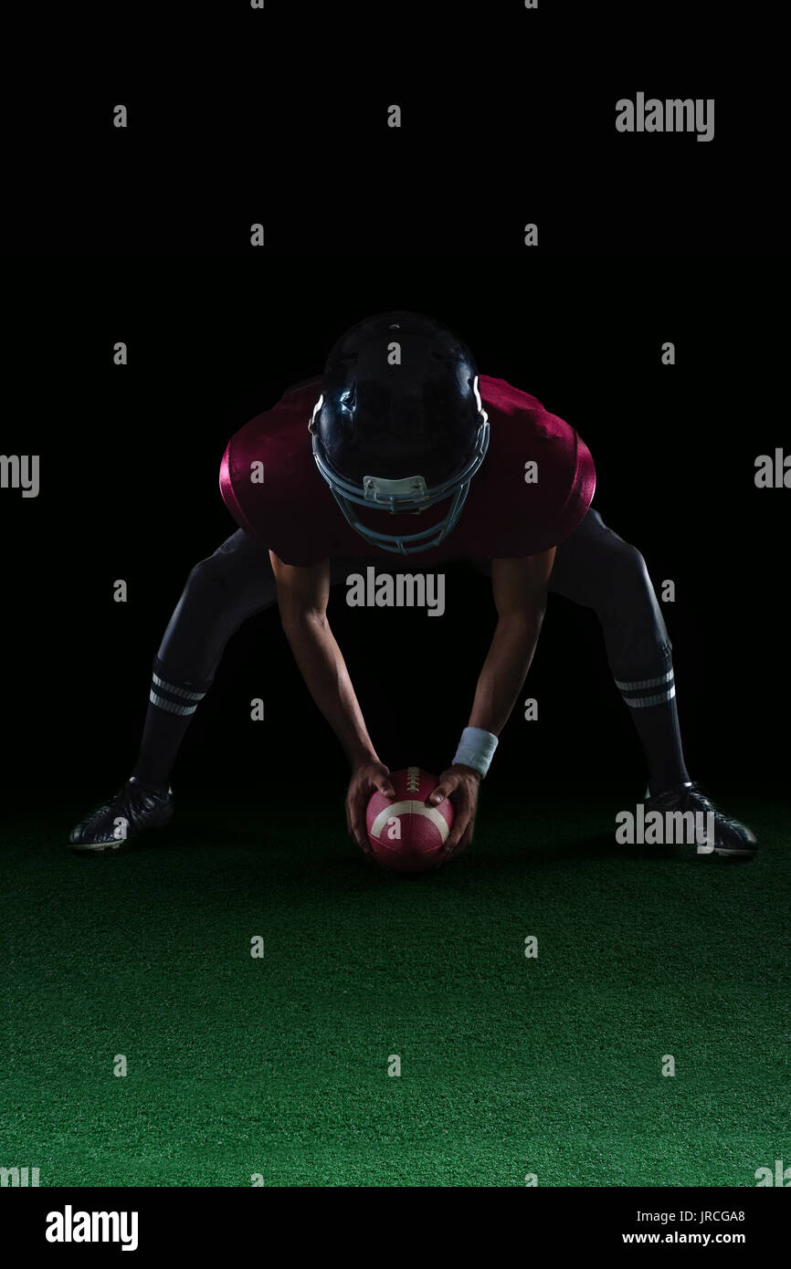 American football player bending holding a ball on turf with both his