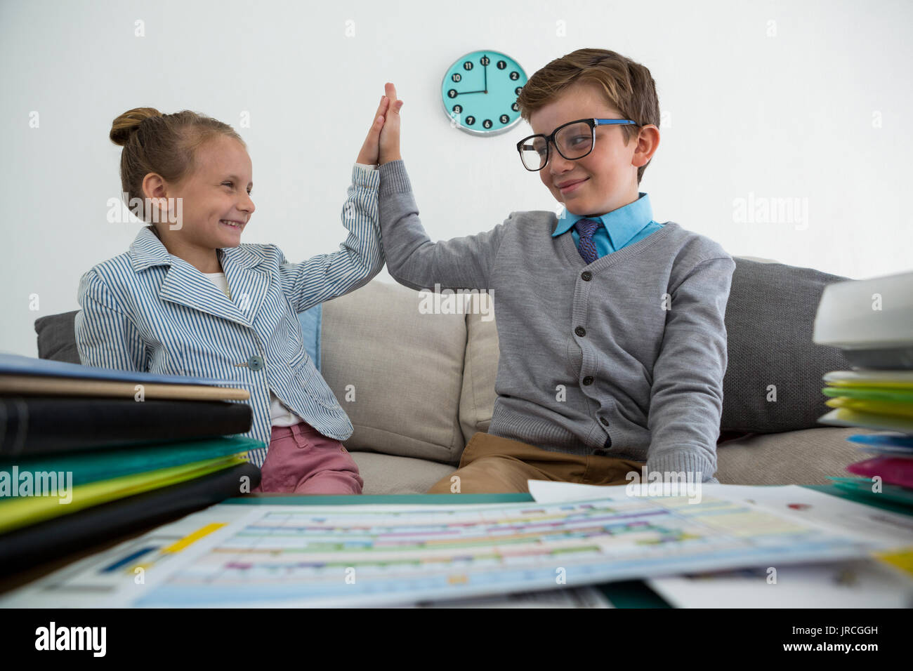 Smiling colleagues giving high five while sitting on sofa in office Stock Photo