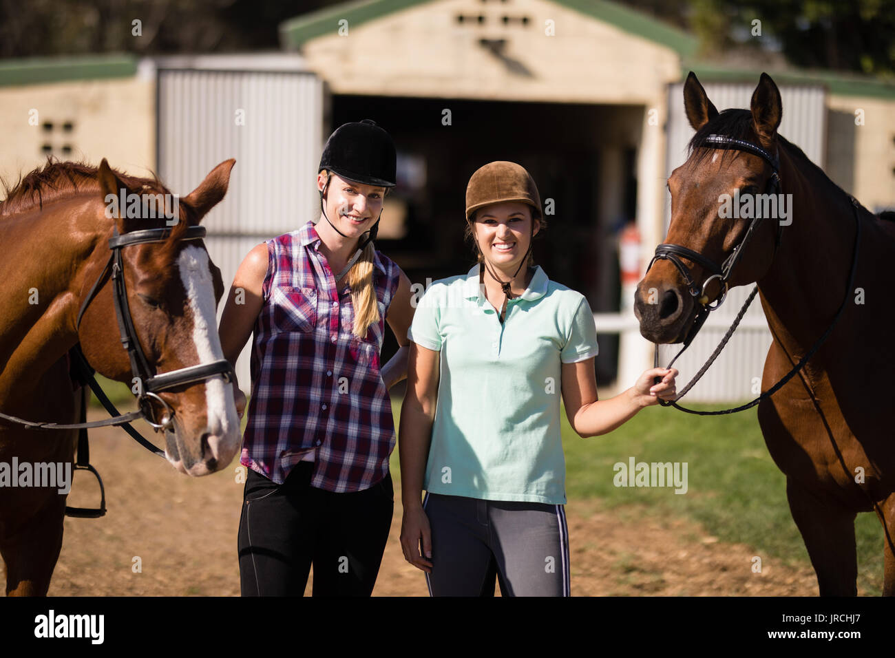 Portrait of smiling friends with horses standing on field at paddock Stock Photo