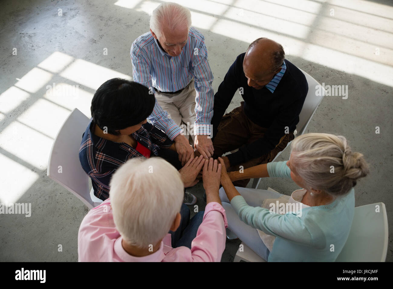 High angle view of senior friends stacking hands while sitting on chair in art class Stock Photo