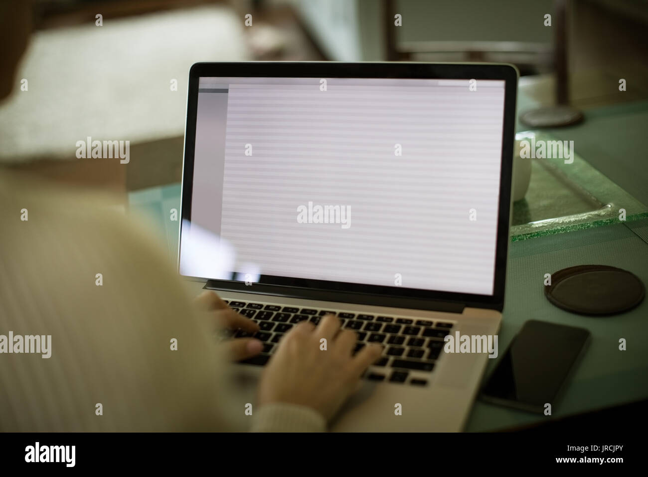 Cropped image of woman using laptop at table in kitchen Stock Photo