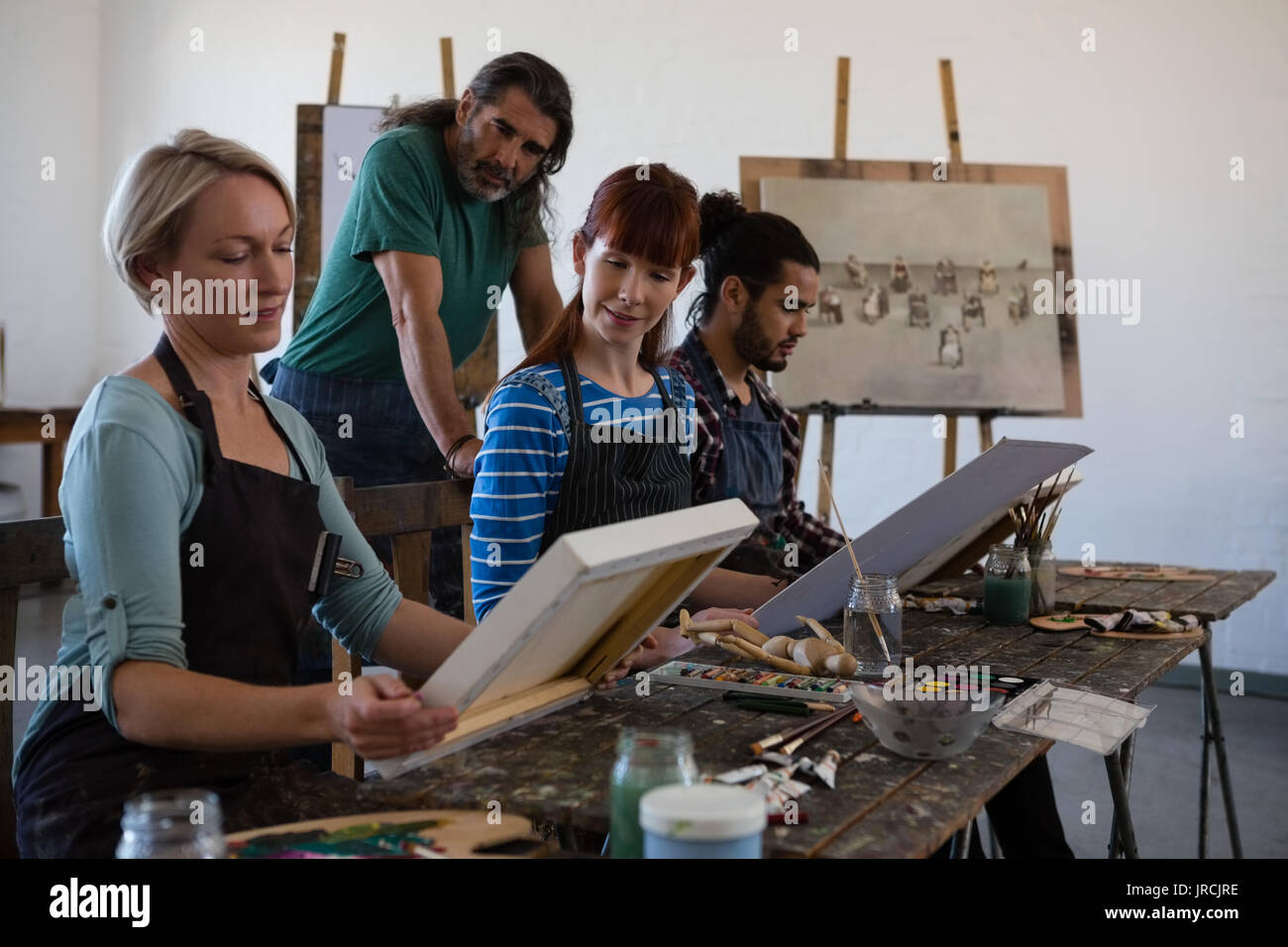 Teacher and student looking woman holding artists canvas in art class ...