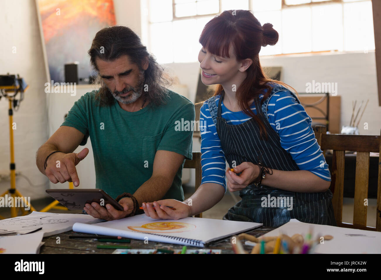 Teacher showing tablet computer to student at table in art class Stock Photo