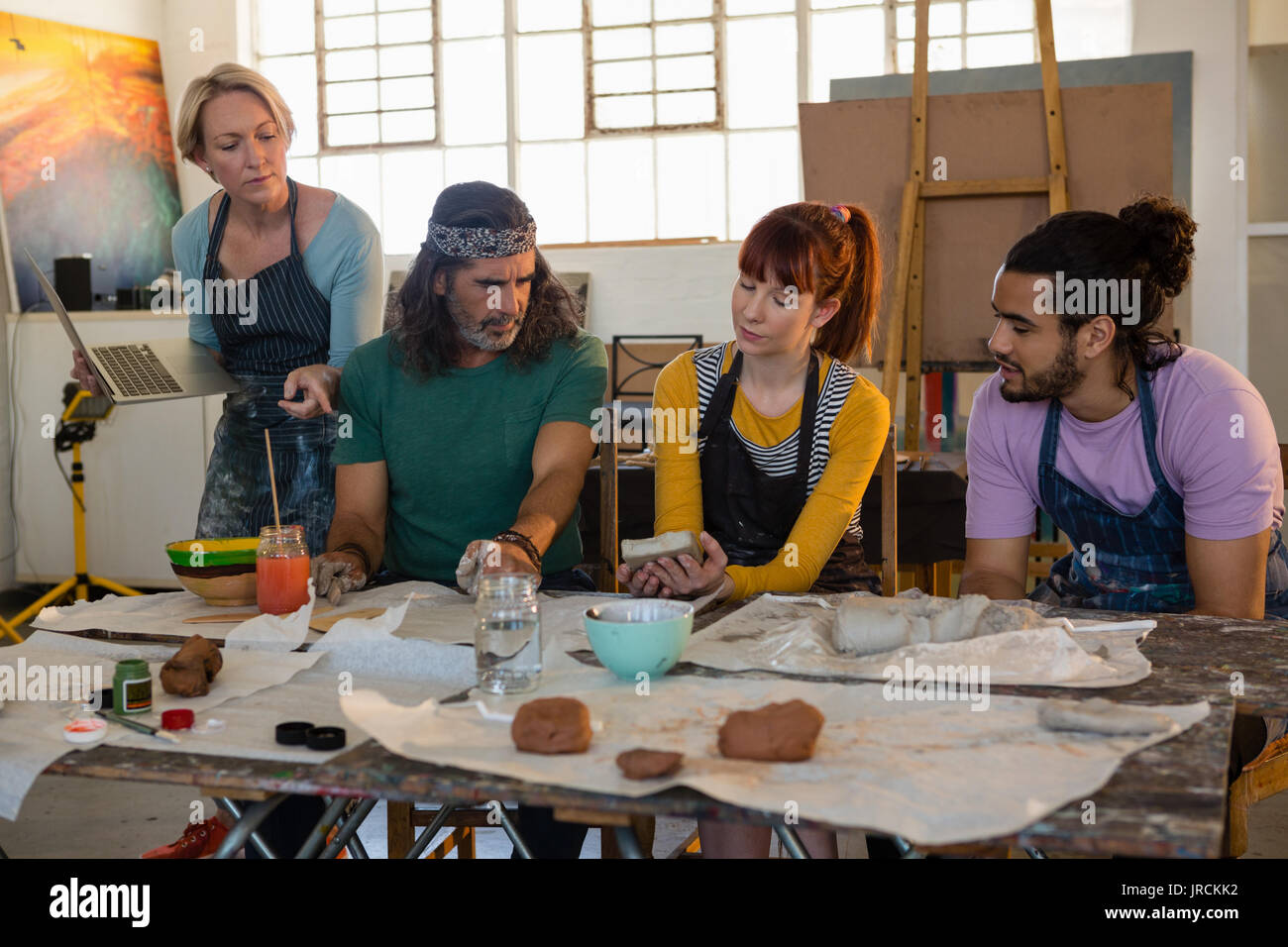 Teacher holding laptop while guiding student in art class Stock Photo