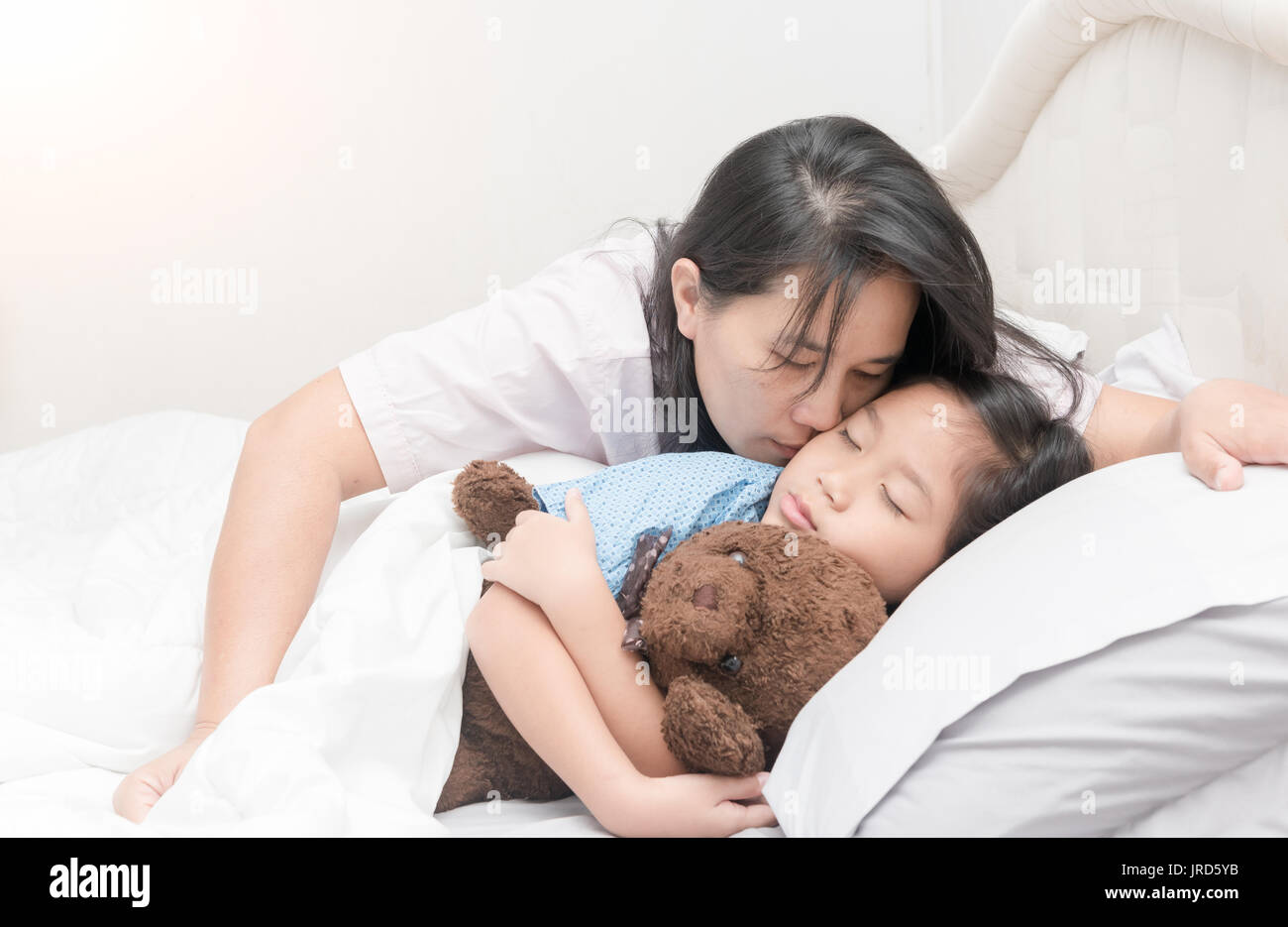Mother is kissing her daughter in cheek while laying on bed on morning in bedroom, love and care concept Stock Photo