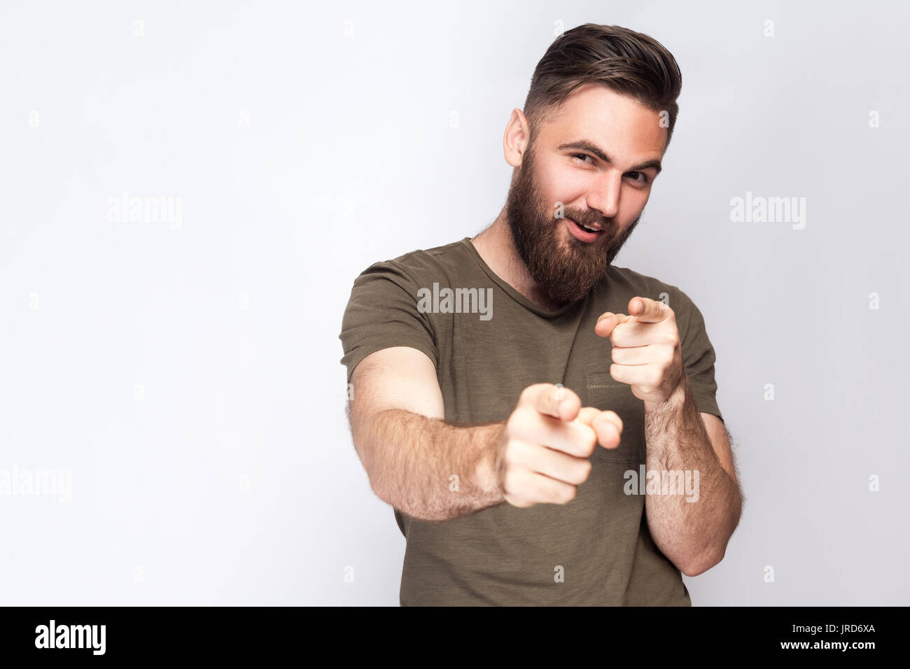 Hey you! Portrait of happy bearded man with dark green t shirt against light gray background. studio shot. Stock Photo