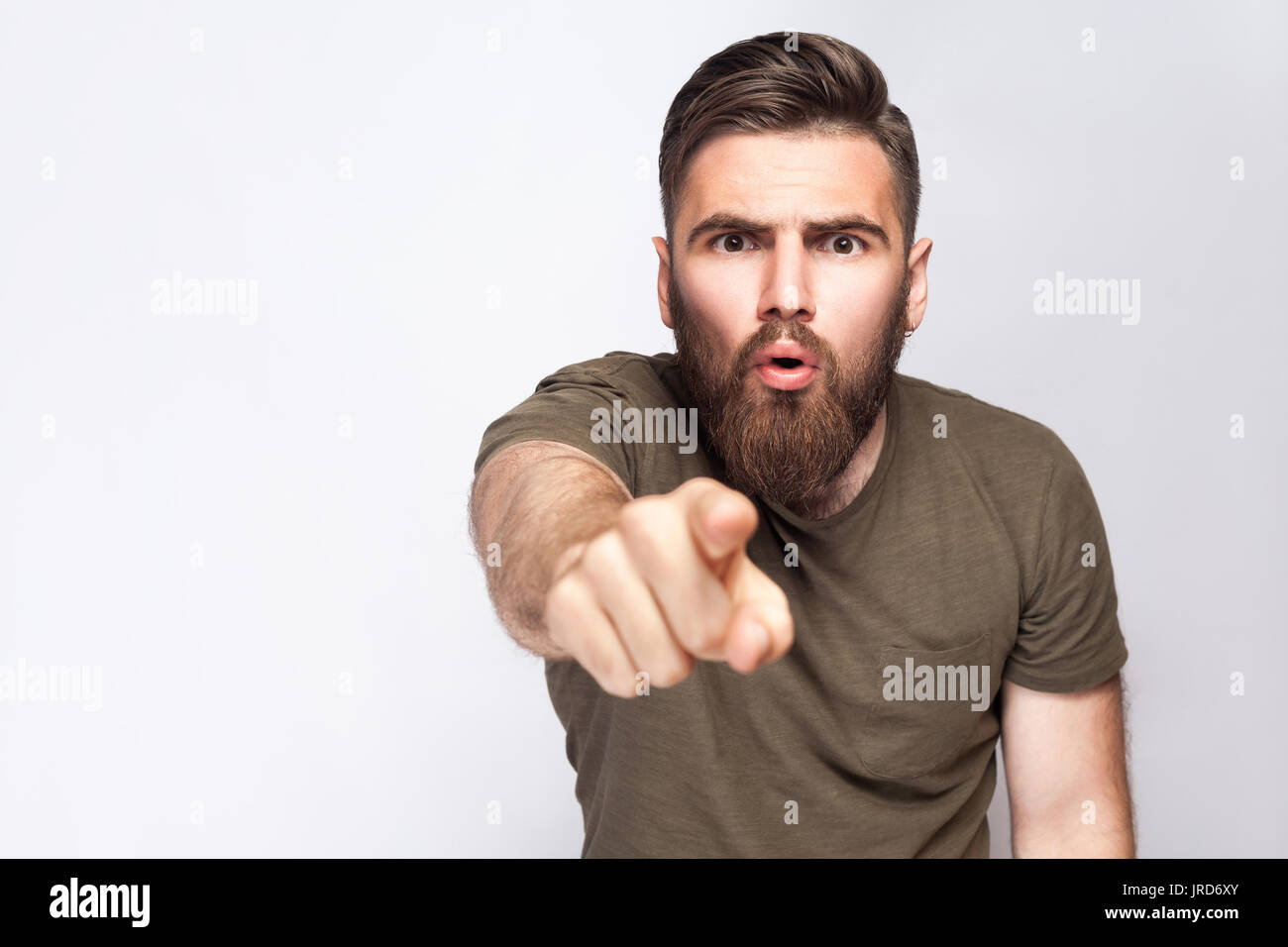 Hey You! Portrait of surprised excited bearded man with dark green t shirt against light gray background. studio shot. Stock Photo
