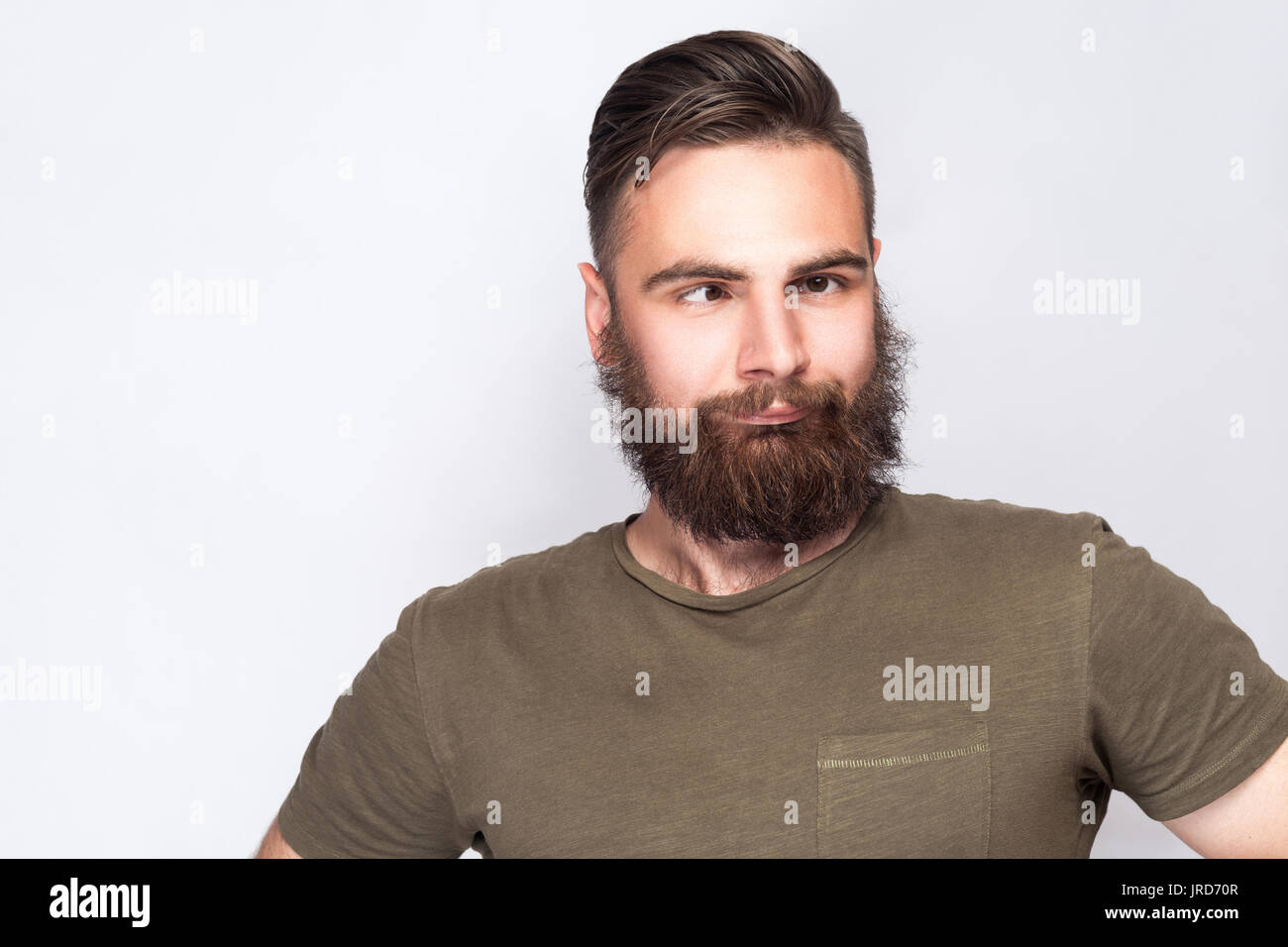 Portrait of crazy cross eyed bearded man with dark green t shirt against light gray background. studio shot. Stock Photo