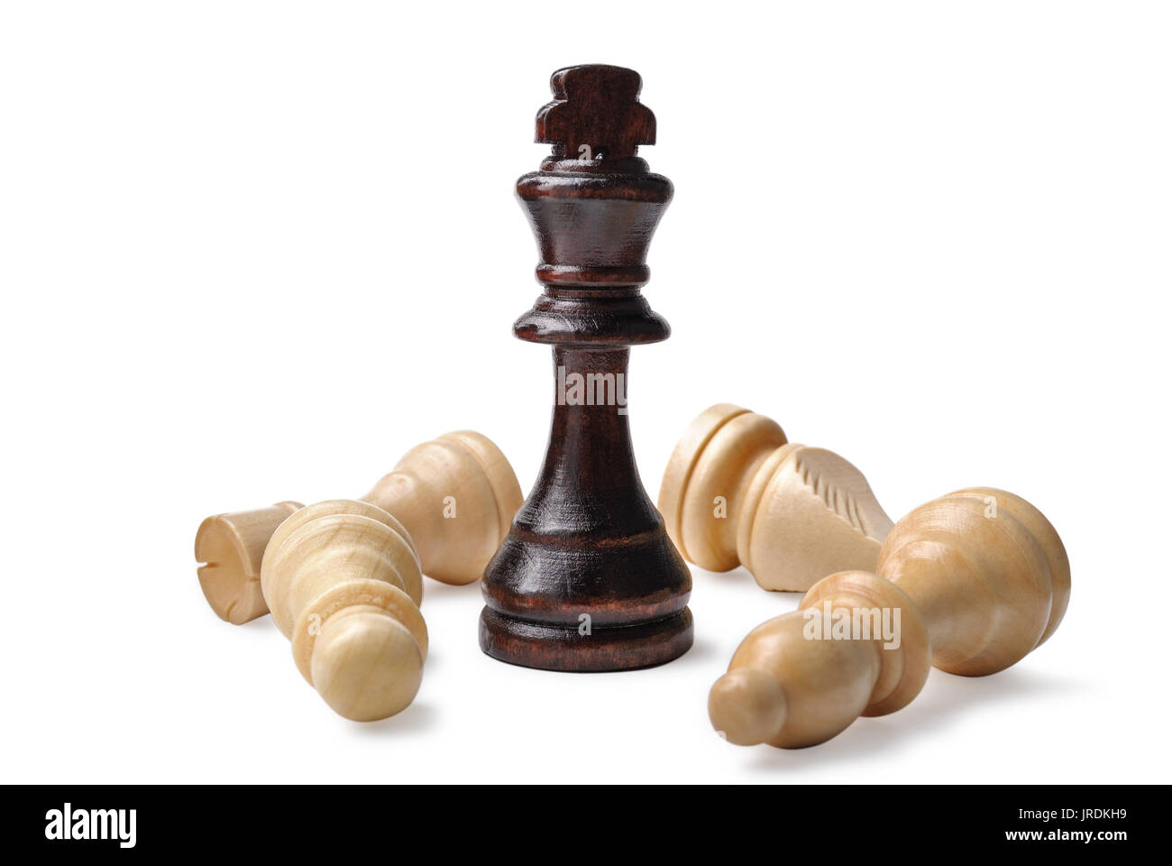 Different wooden chess pieces with a victorious dark king standing upright over several lighter opponents on a white background Stock Photo