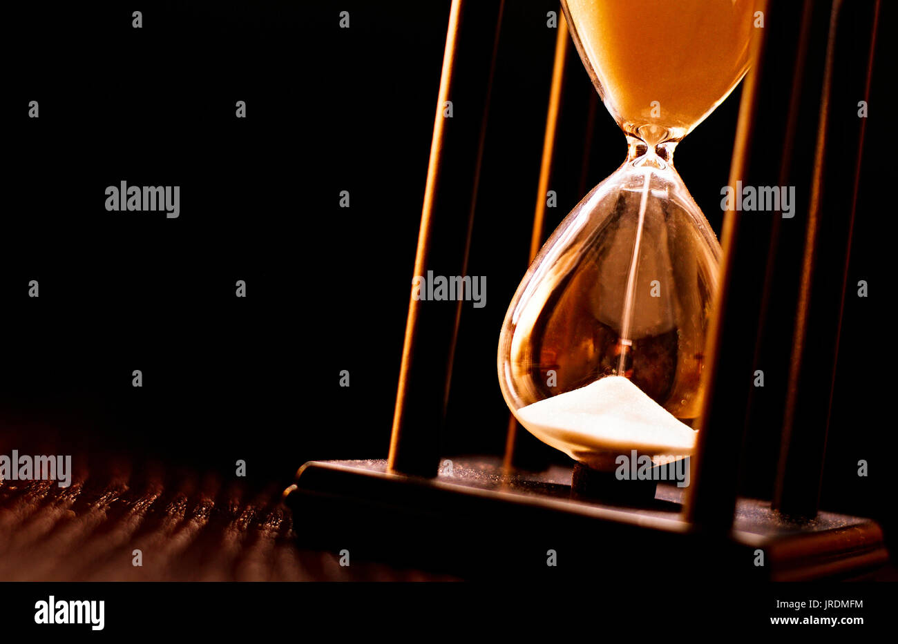 Newly turned hourglass with running sand measuring the passing time to a deadline or expiry of a fixed time period, close up on a dark background Stock Photo