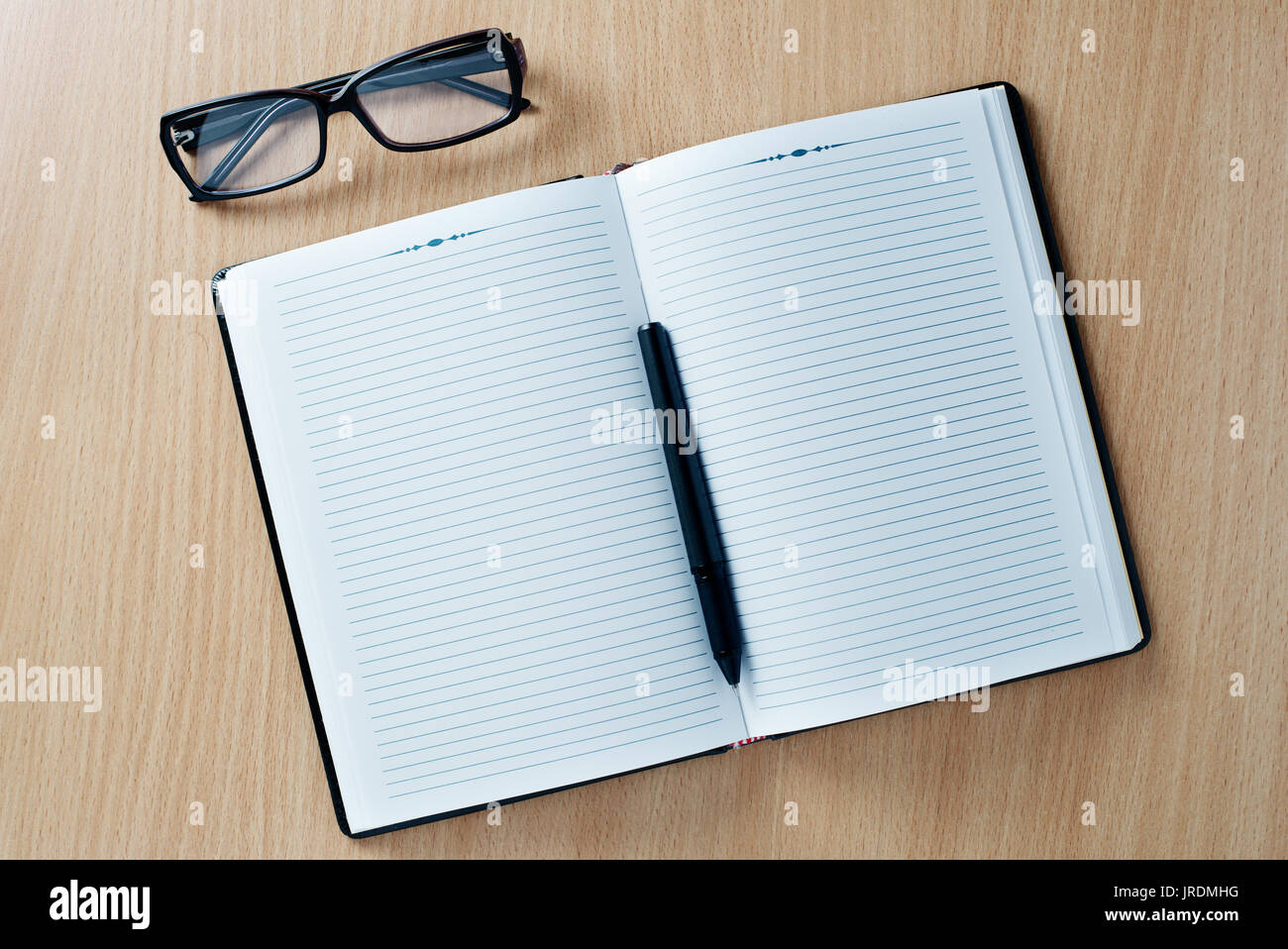 Open diary or office journal with a double page lined blank spread for your text with a ballpoint pen and glasses on a wooden desk, overhead view Stock Photo