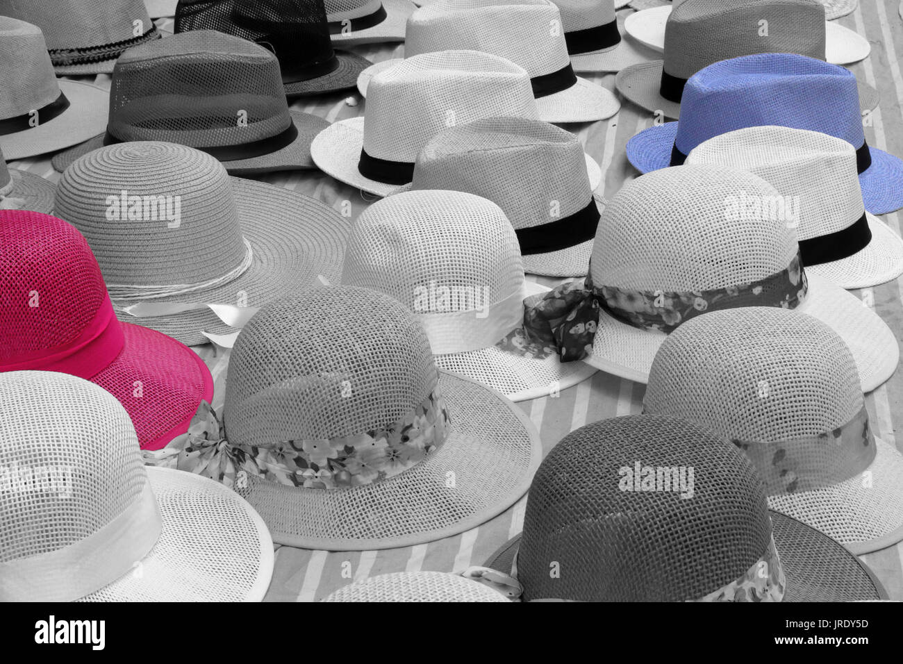 A close view of many Panama straw hats on a cotton sheet on sale on a street by a peddler. All black and white except one red hat and one blue hat Stock Photo
