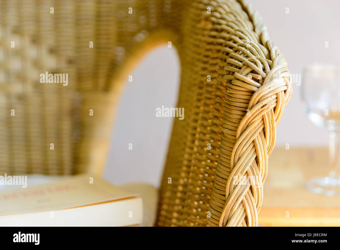 Close-up view on the armrest of a rattan chair with a white cushion, a book and a glass of water. Stock Photo